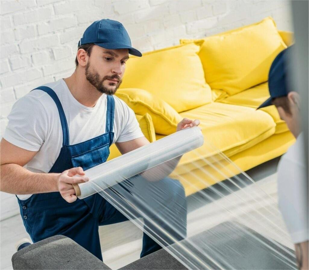 mover-wrapping-couch-with-roll-of-stretch-film-in-apartment-1025x1536