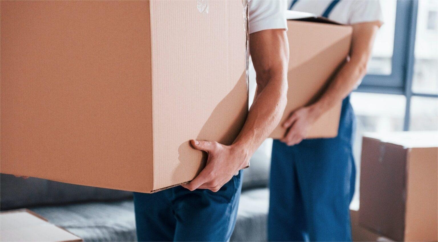 with-boxes-in-hands-two-young-movers-in-blue-uniform-working-indoors-in-the-room-1536x932